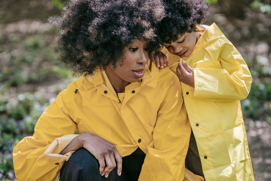 A mother and child sharing a tender moment outdoors, both wearing matching yellow raincoats.