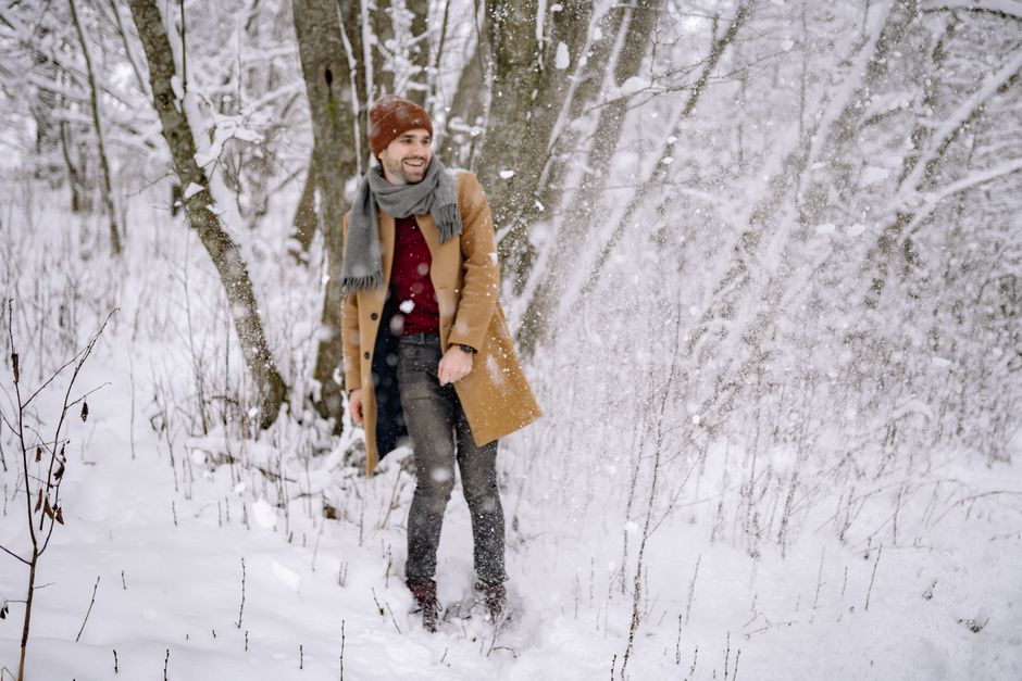 A happy man standing in a snowy forest, bundled up in winter clothes, enjoying the snowfal