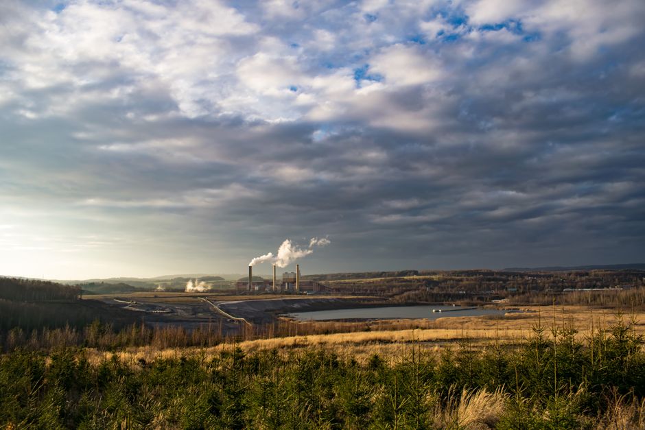 Power plant in Březová, Czechia with smoke stacks, lake, and cloudy sky.