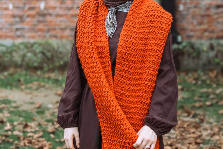 Close-up of a woman wearing a vibrant orange knit scarf, exuding elegance and style outdoors.