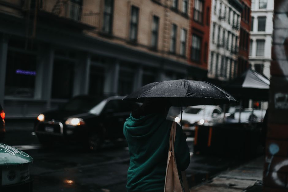 Back view of unrecognizable person in casual clothes walking with umbrella on city street