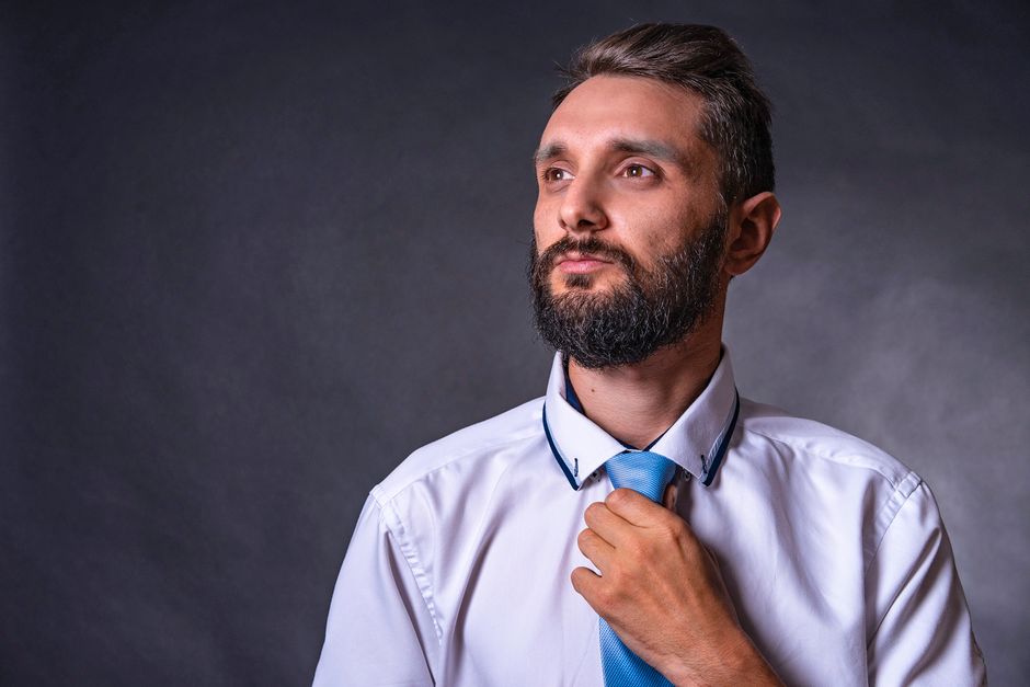 Portrait of a confident bearded man in a studio setting adjusting his necktie. Professional and poised.