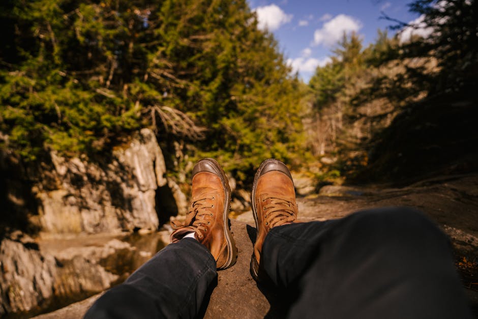 Crop legs of anonymous traveler lying on rocky cliff in green woods in sunny day