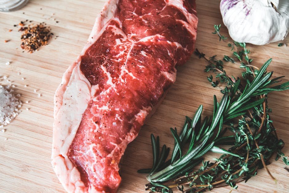 Close-up of fresh raw beef steak with rosemary, thyme, garlic, and spices on a wooden board.