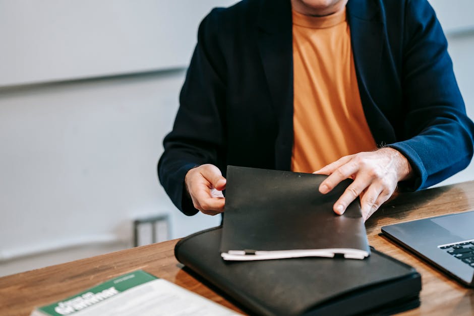 A business professional in a blazer organizing documents at a wooden desk inside an office.