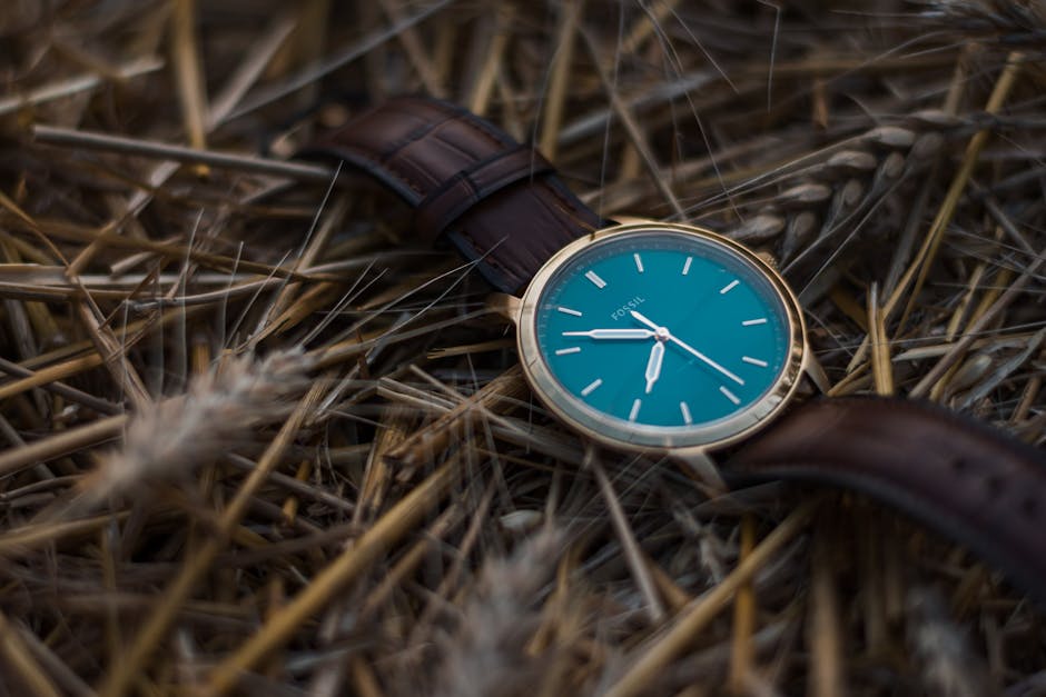 Elegant Fossil watch with teal face and leather band laid on a rustic wheat field, showcasing luxury and nature.