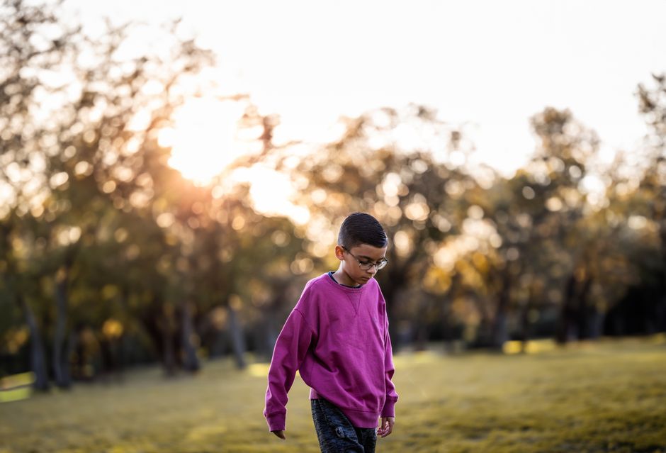Boy in pink sweatshirt walking outdoors in a sunny park during autumn with golden light an