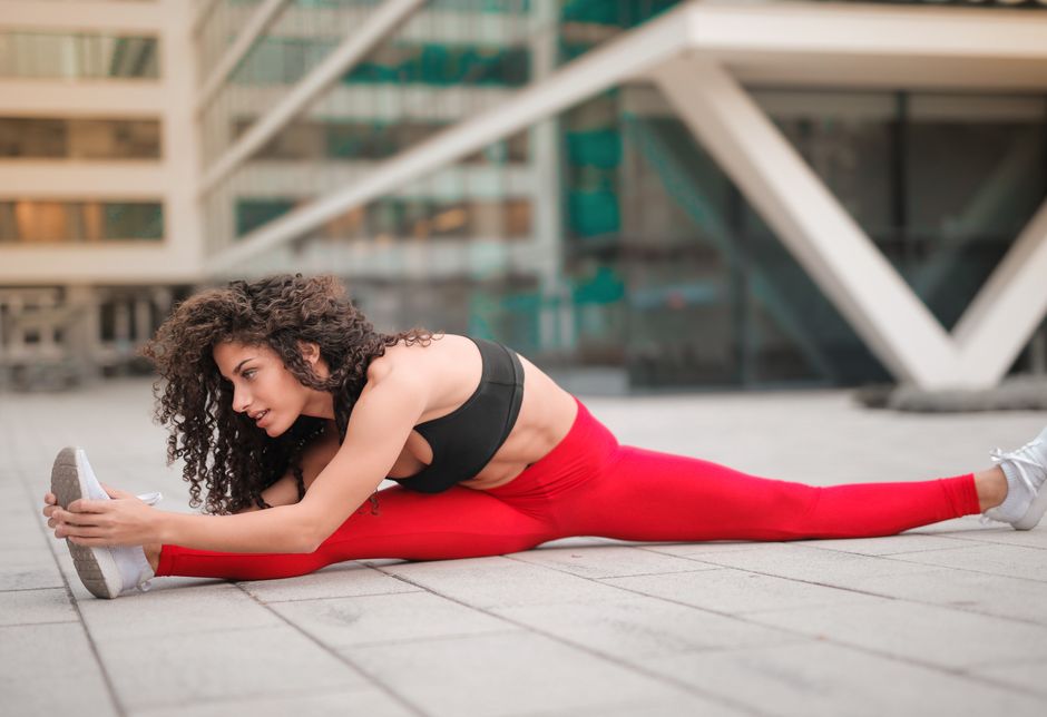 A woman performs a stretching exercise in an urban environment, showcasing flexibility and fitness.