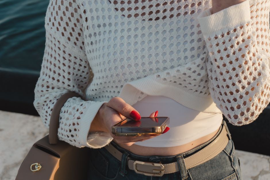 Close-up of a woman checking her smartphone in casual, stylish attire with bright sunlight.