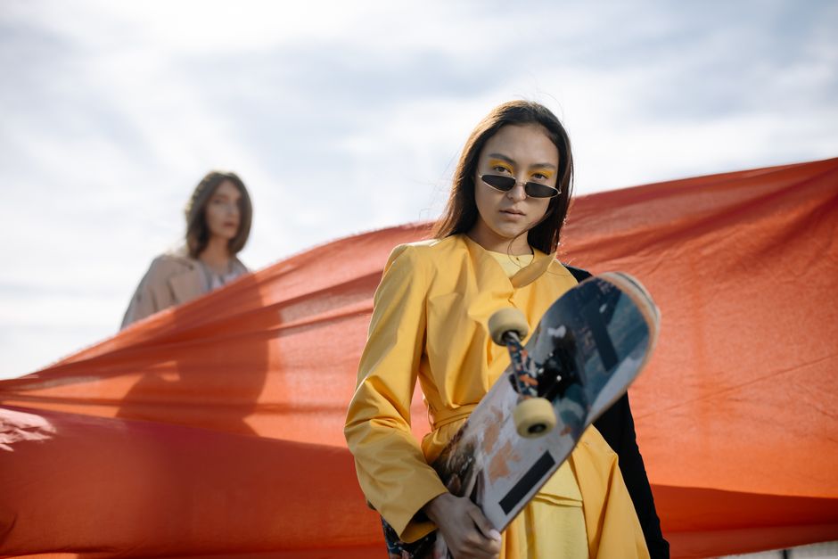 Two stylish women posing with a skateboard against a vibrant backdrop, highlighting modern fashion flair.