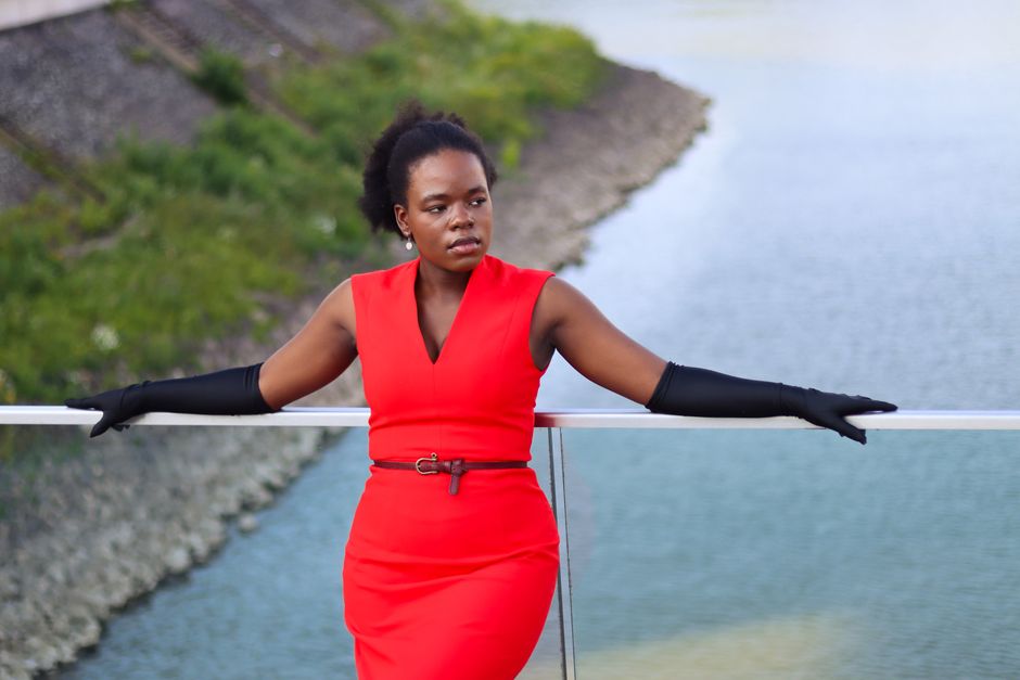 Elegant woman in a red dress with black gloves posing by Düsseldorf's waterfront, exuding confidence and style.
