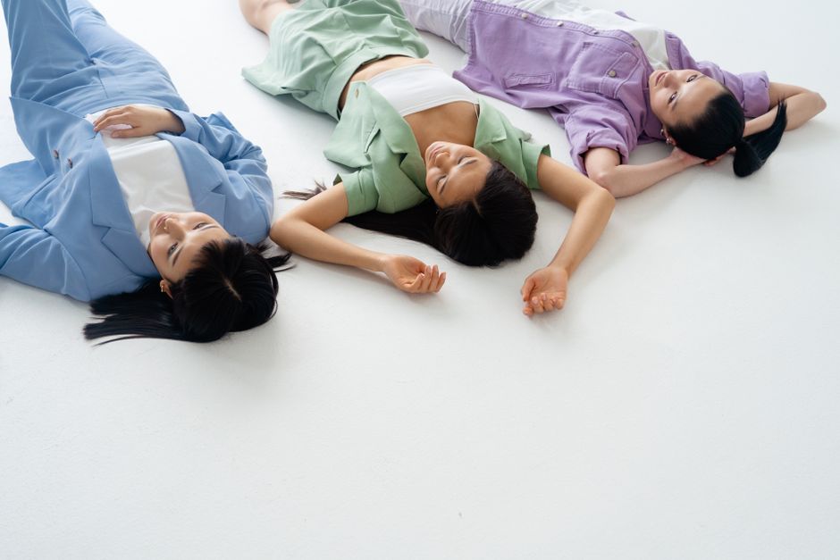 Three women in pastel jackets lying on a white floor, representing friendship and relaxation.