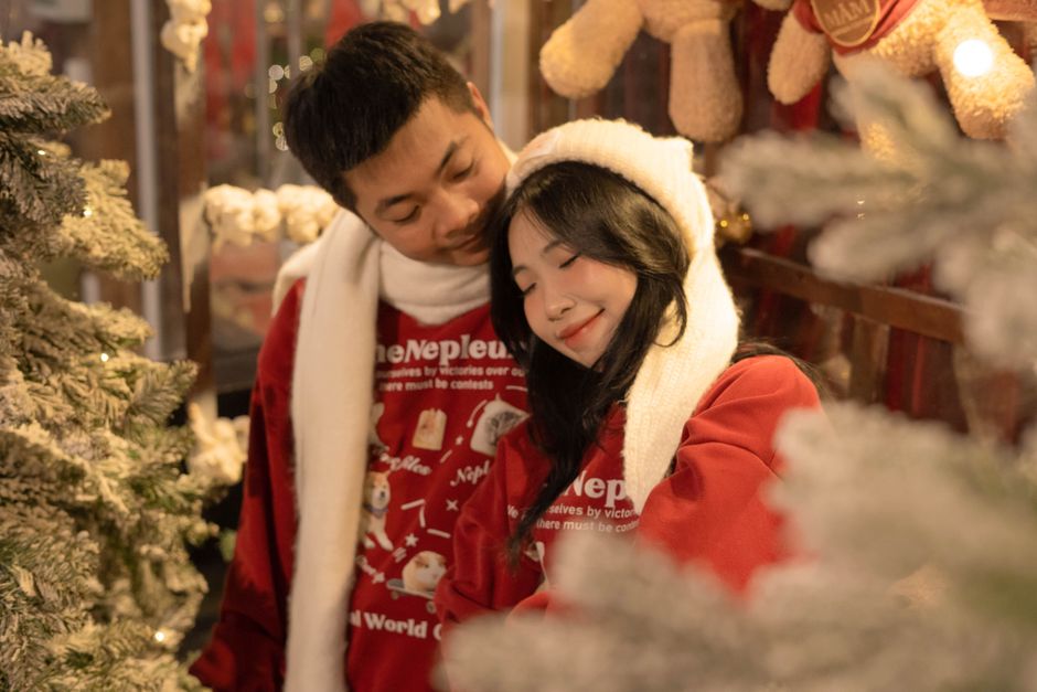 A couple in winter attire enjoying a cozy moment near a decorated tree indoors.