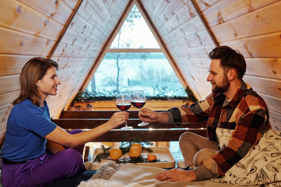 Couple enjoying red wine in a cozy cabin, celebrating winter indoors together.