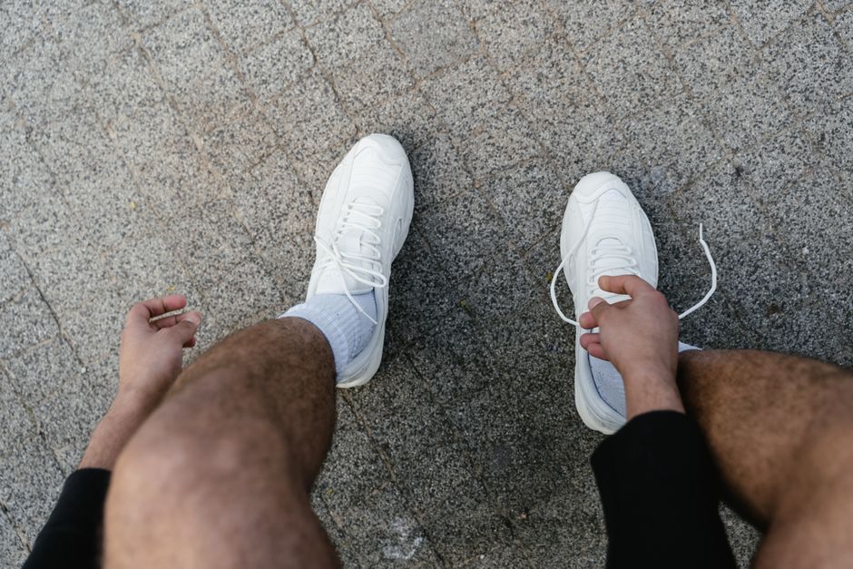 Close-up of a young adult tying white sneakers on a paved surface.