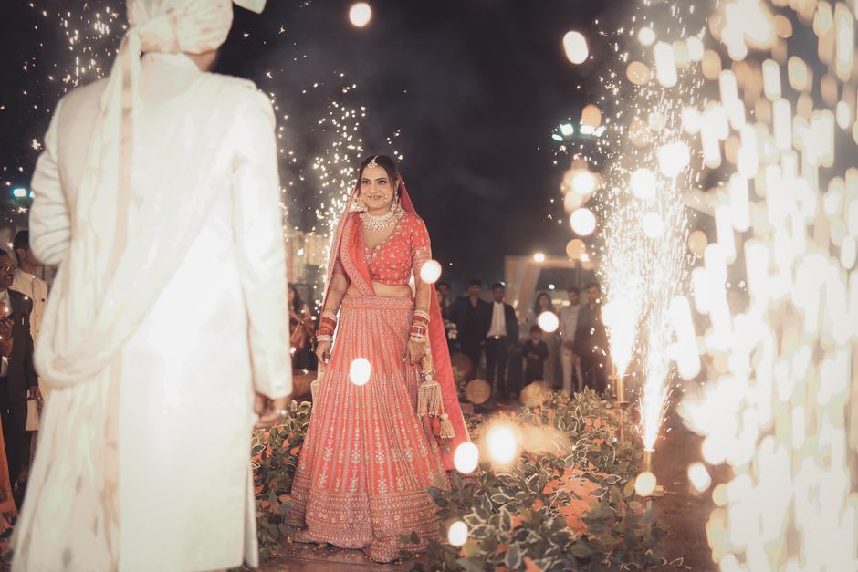 Nighttime wedding scene captures a bride in vibrant attire amidst sparkling fireworks.