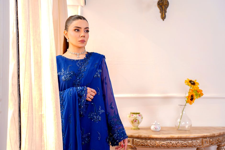 Model in blue chiffon dress by window indoors. Elegant, traditional style.