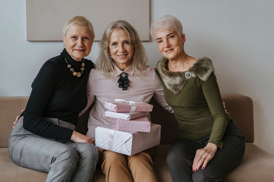 Three senior women sitting together with gifts, celebrating friendship indoors.