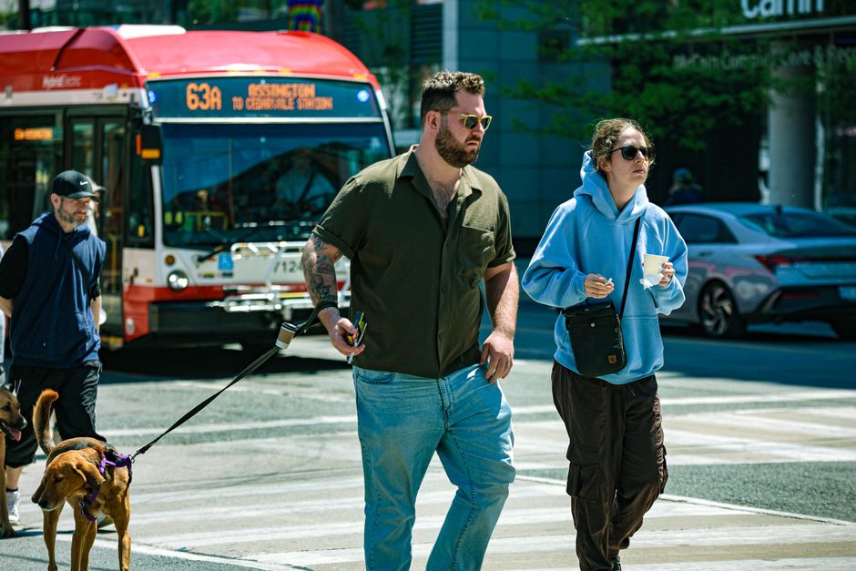 People crossing the street in an urban setting with a city bus and dog in the background.