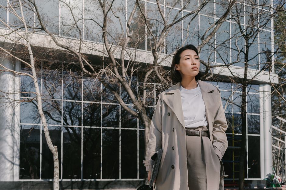 Fashionable woman in gray coat stands confidently outdoors against sleek building backdrop