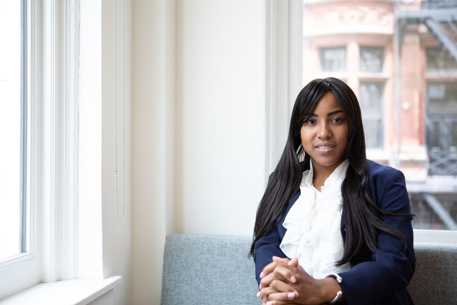 Elegant woman in formal attire seated by a large office window, exuding confidence.