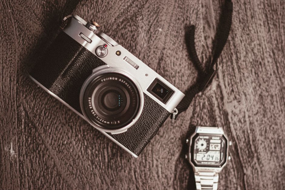 A flat lay of a vintage camera and classic watch on a textured wooden surface.