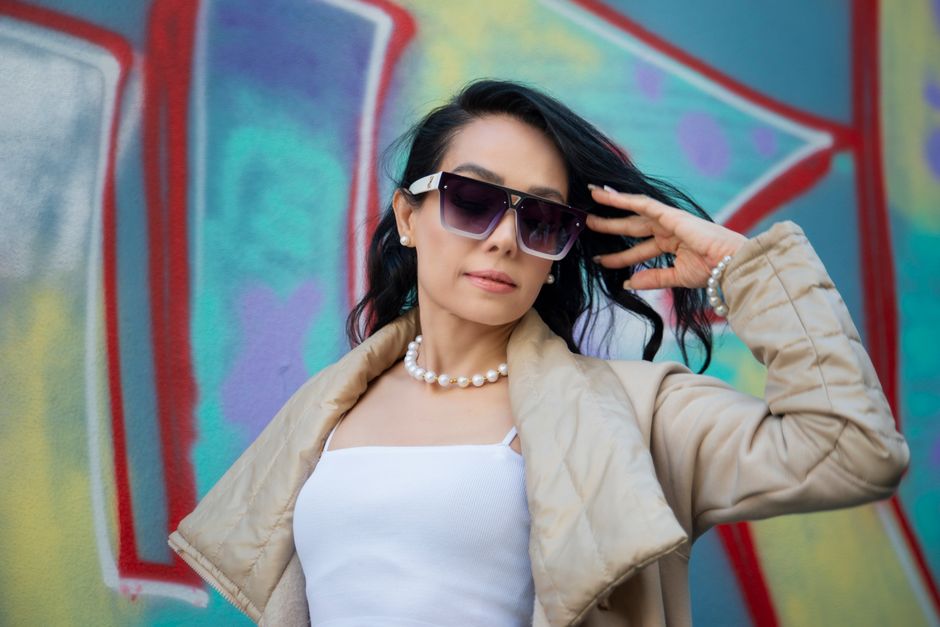 Confident woman posing with sunglasses in front of vibrant graffiti wall.