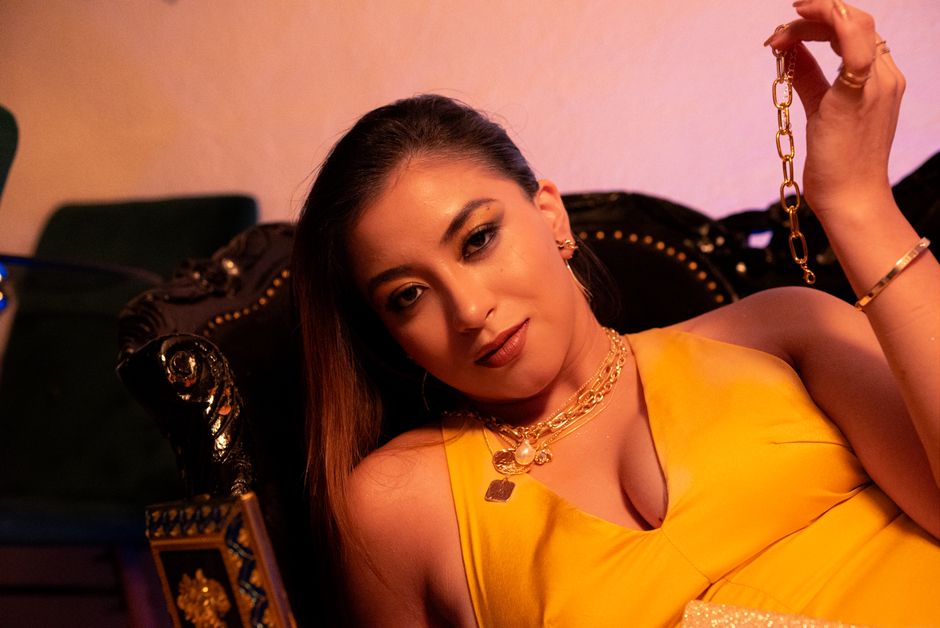 Stylish woman lounging indoors in a vibrant yellow dress and gold jewelry.