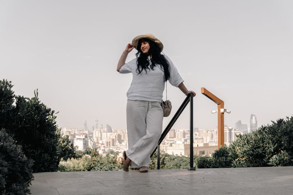 A woman in white attire enjoys a sunny day with a view of Baku skyline.