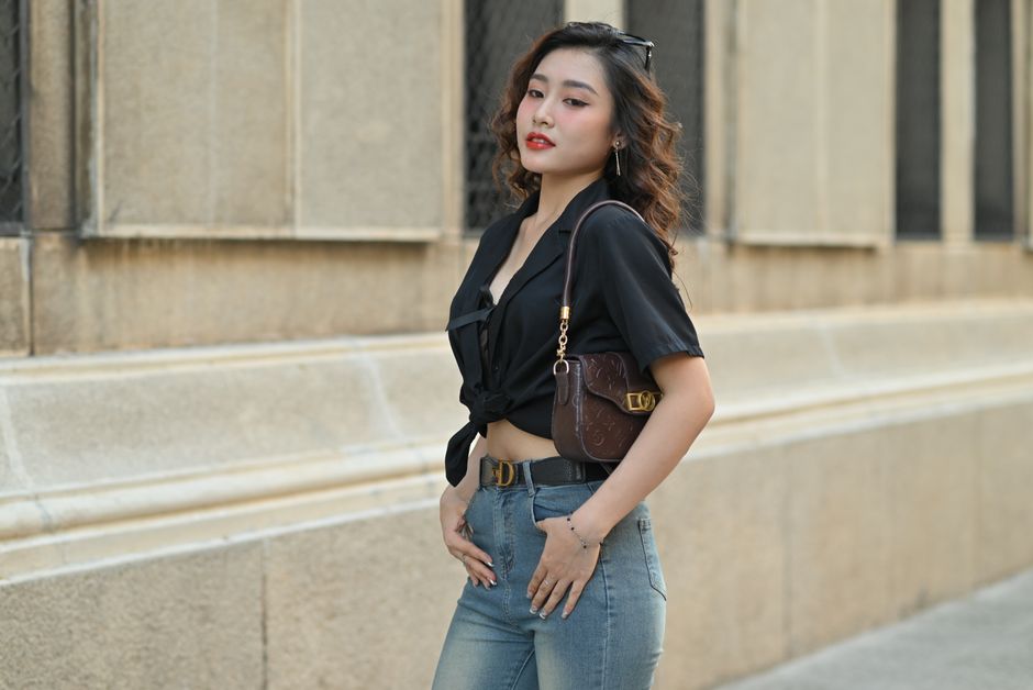 Fashionable person in jeans and black top posing outdoors near a building.