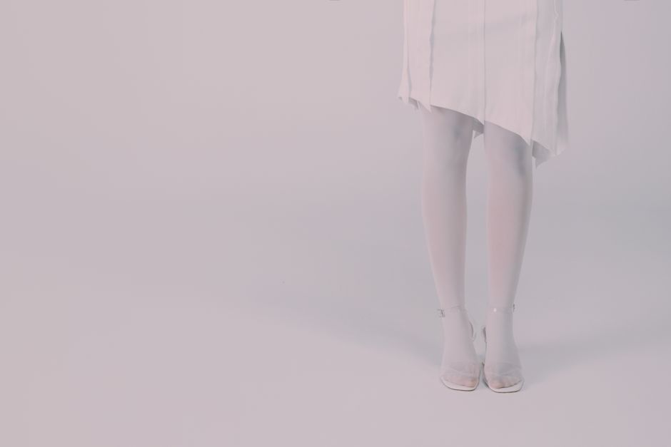 Close-up of a woman's legs wearing a white dress and high heels in a studio setting.