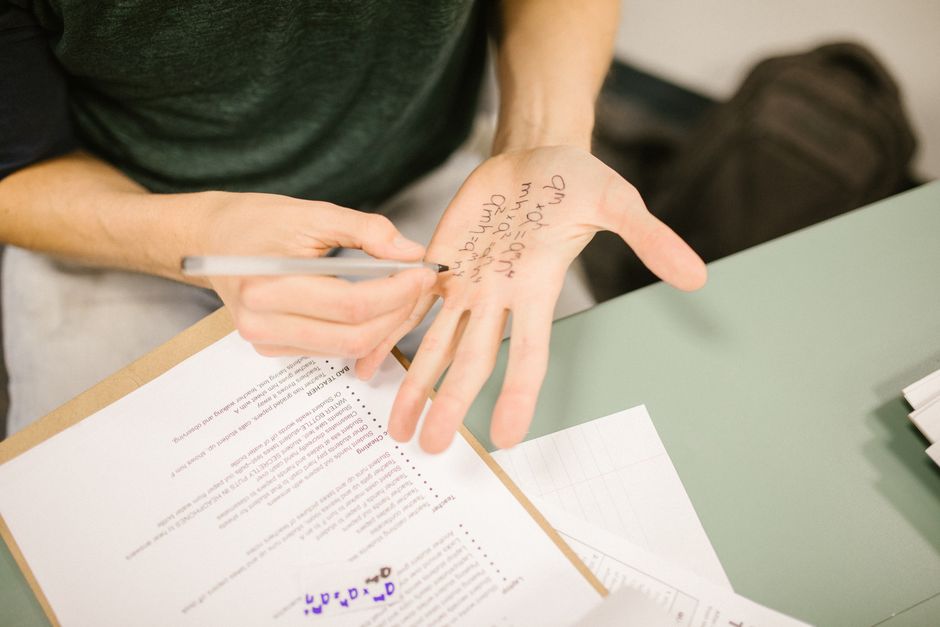 A student discreetly writes notes on their palm during an exam to aid in cheating.