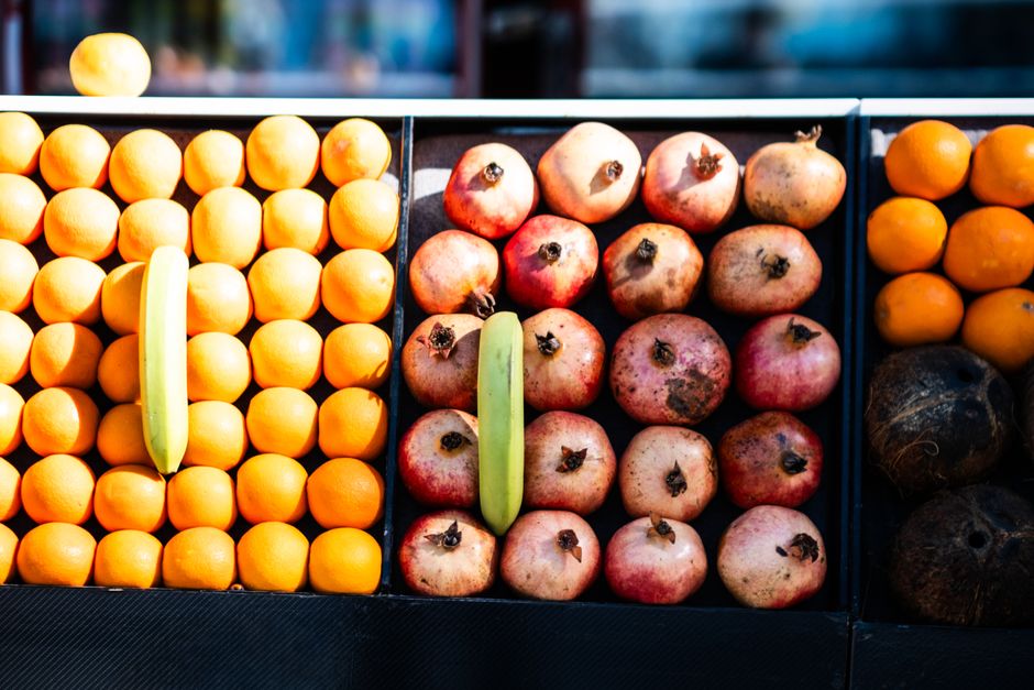 Colorful rows of fresh fruits including oranges, pomegranates, and bananas at a market.