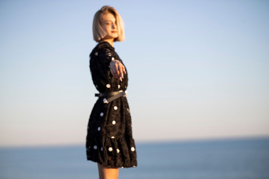 Fashionable woman posing by the sea in a black dress during a sunny day.