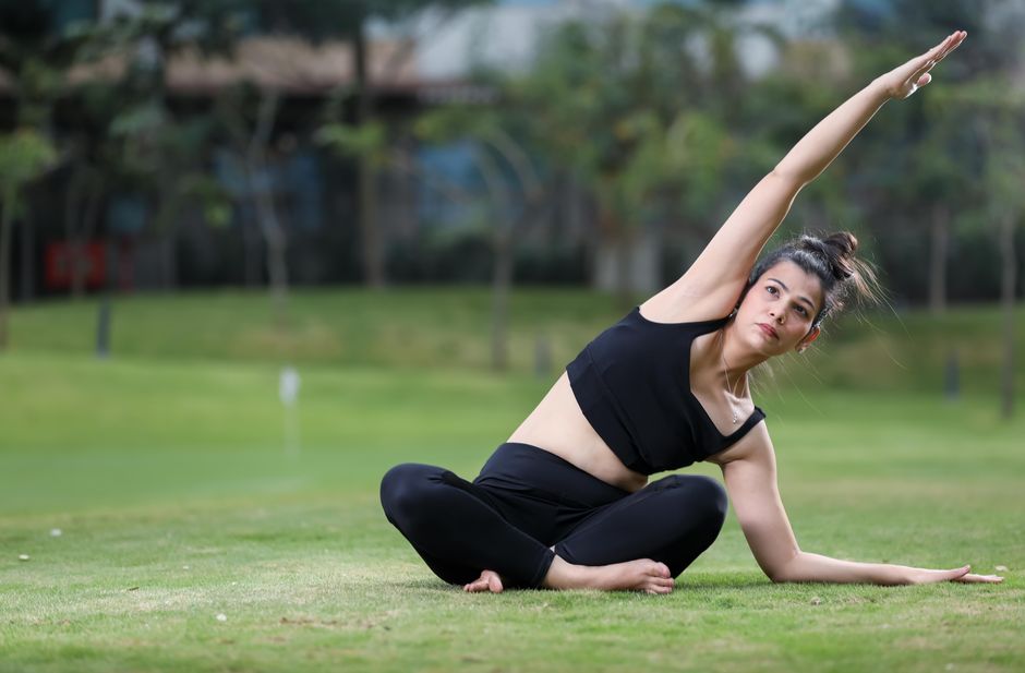 A young woman performing a yoga pose on a grassy field in a serene park setting.