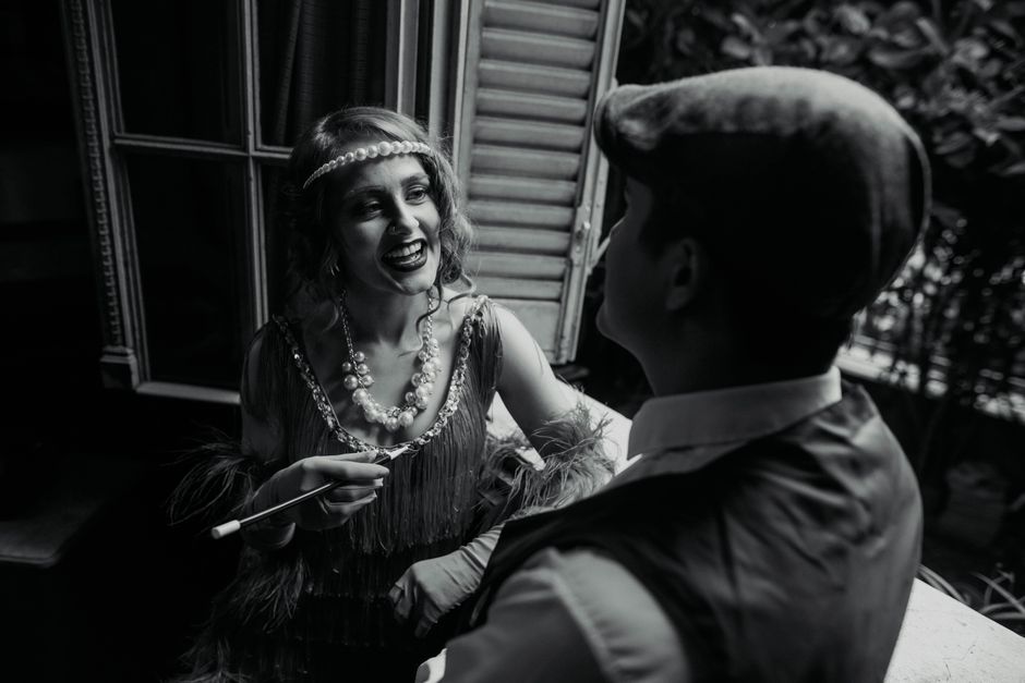1920s style couple laughing near window in Buenos Aires, exuding vintage elegance and charm.