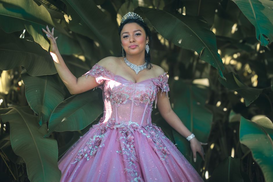 Young woman in a pink quinceañera dress surrounded by lush green leaves.