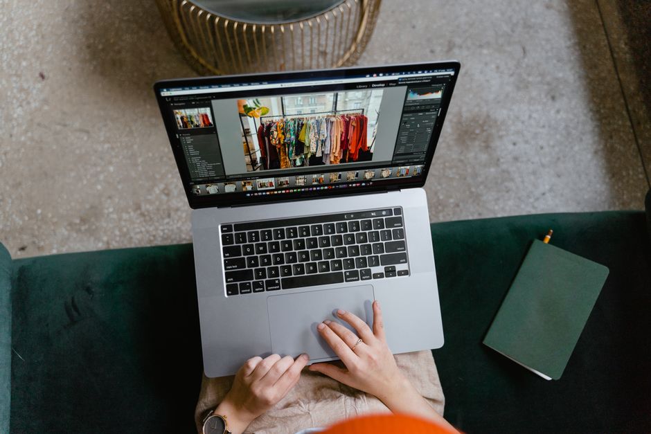 Person editing clothing photos on a laptop indoors, showcasing online fashion business or