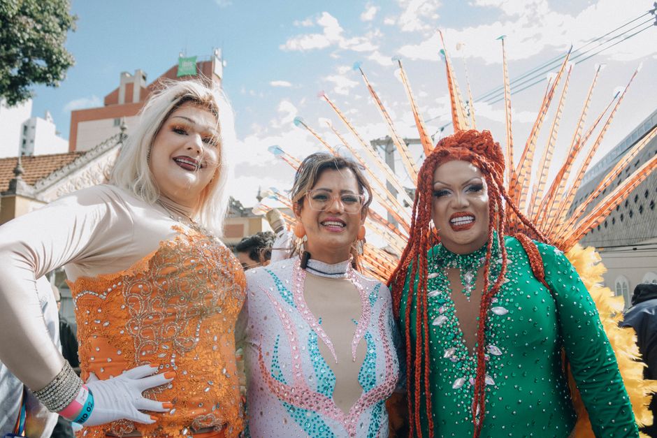 Three people celebrate in vibrant costumes at an outdoor event, exuding joy.