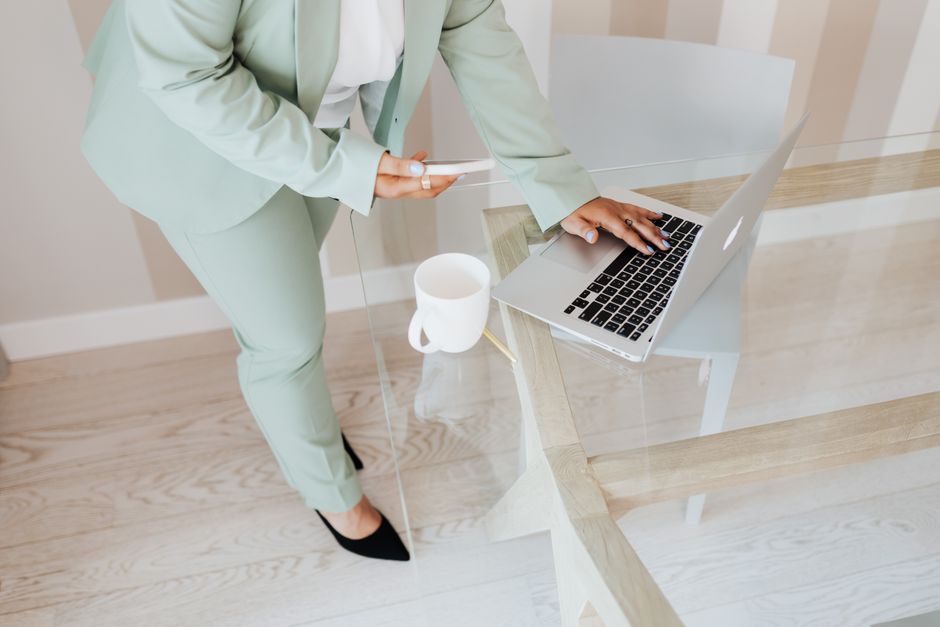 Person in a suit using a laptop and smartphone at a glass table in a modern office setting.