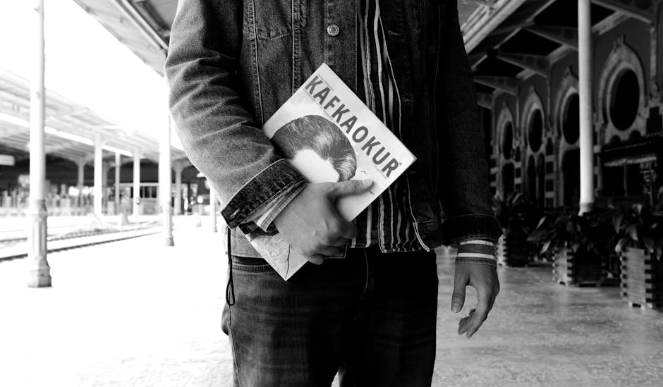 A man in denim jacket holds a Kafkaokur magazine at an Istanbul train station.