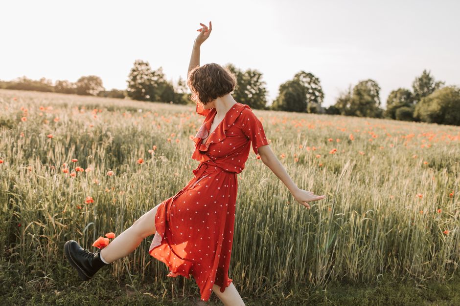 A joyful woman in a red polka dot dress dancing in a sunny field of flowers.
