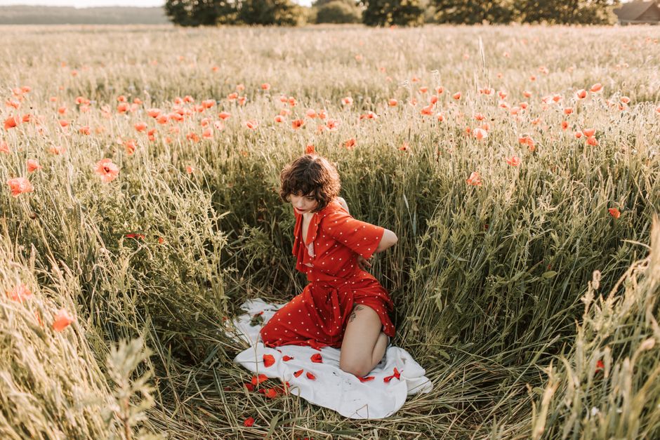 A woman in a red dress kneels amid blooming poppies in a sunlit meadow.