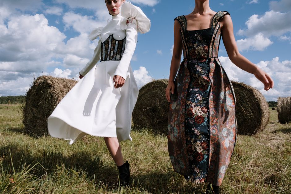Stylish models in elegant dresses posing with hay bales under a bright sky.
