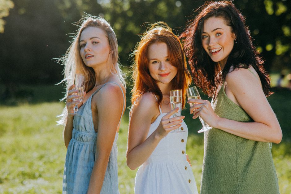 Three women smiling and holding champagne glasses outdoors on a sunny day.