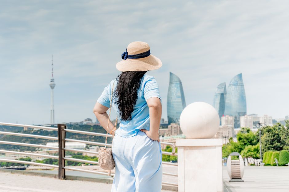 Woman in sunhat admiring Baku city skyline featuring iconic Flame Towers on a sunny day.