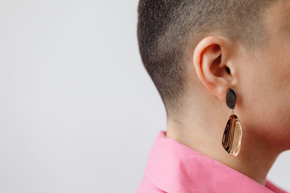 Close-up profile of a woman with a buzzcut wearing a sleek earring on a white background.