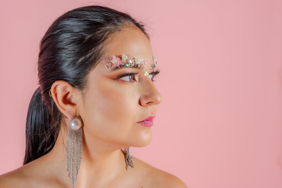 A striking portrait of a stylish woman with creative makeup against a pink background.