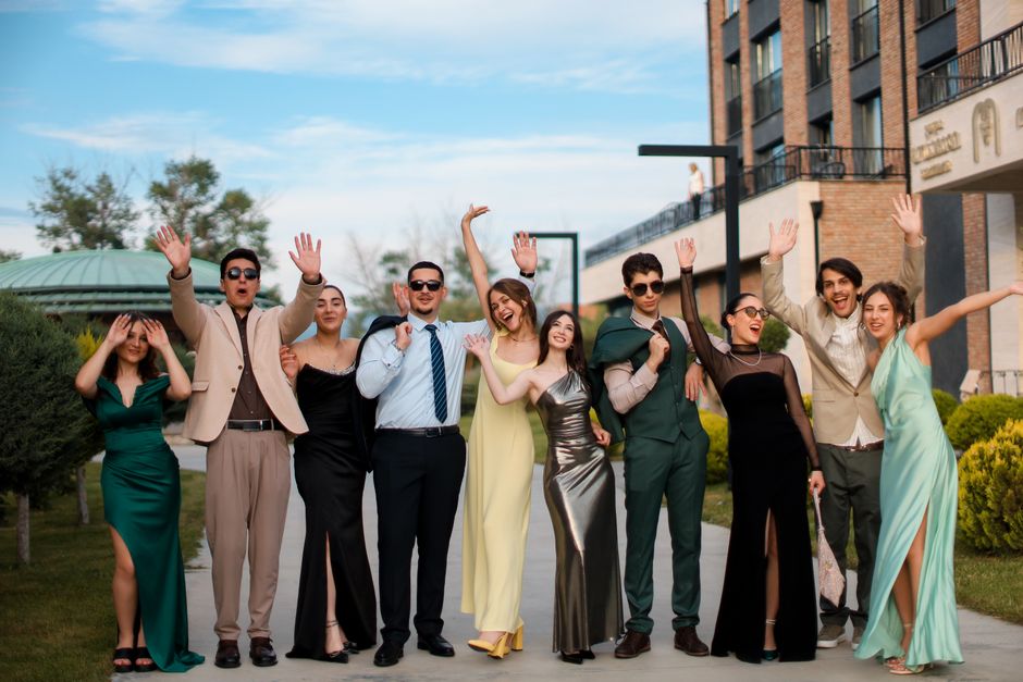 A group of young adults in formal wear enjoying an outdoor photoshoot with vibrant expressions.