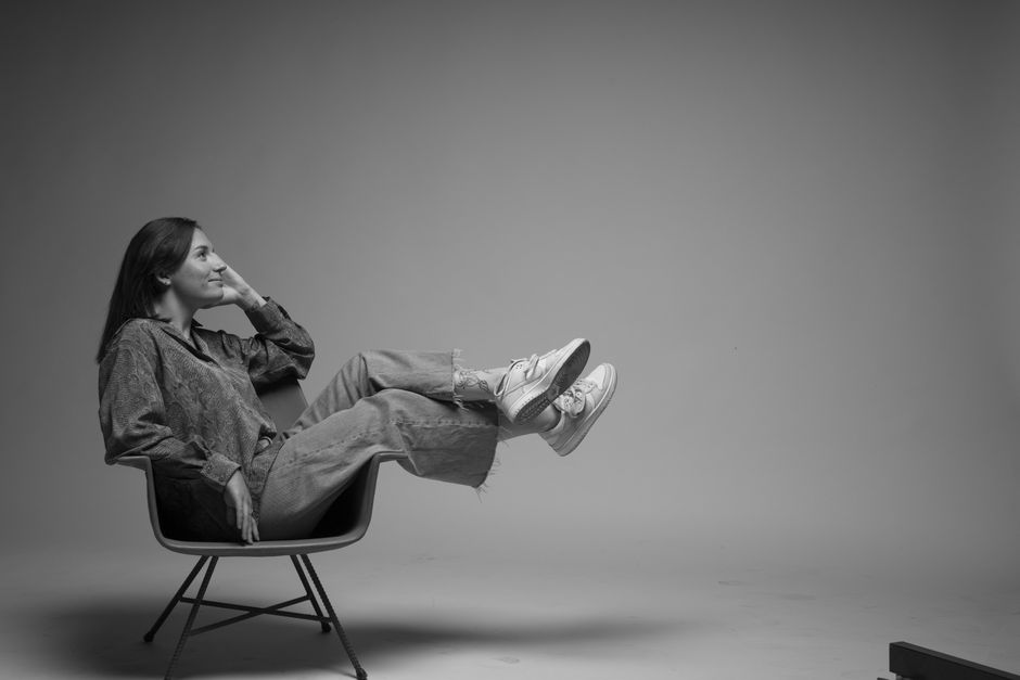 A monochrome portrait of a woman lounging on a chair, dressed in casual denim attire.